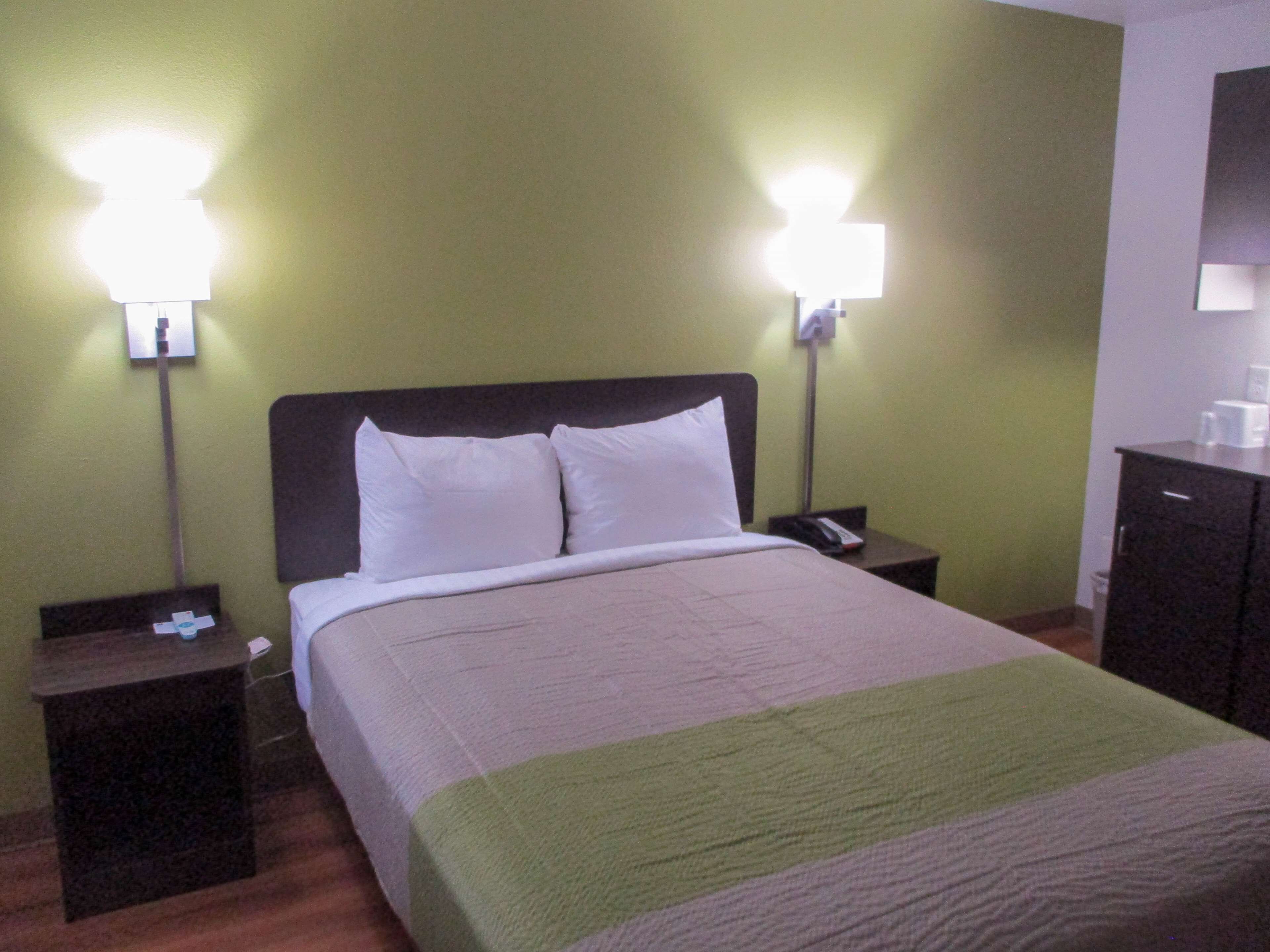 Une chambre d’hôtel comprenant un lit, deux tables de chevet, une commode, une lampe et un placard.