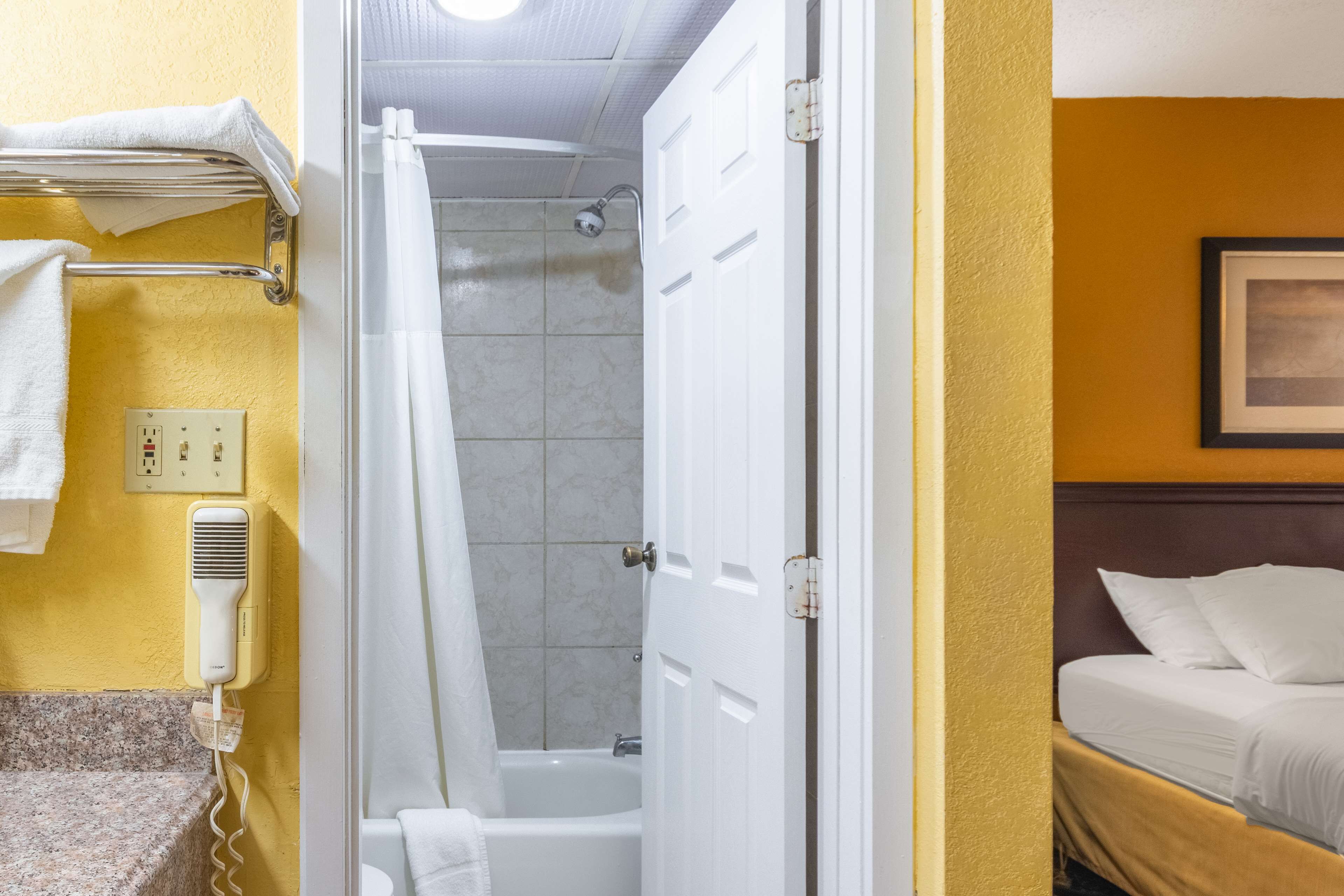 A hotel room with a bathroom containing a shower, bathtub, and a hairdryer on the wall.