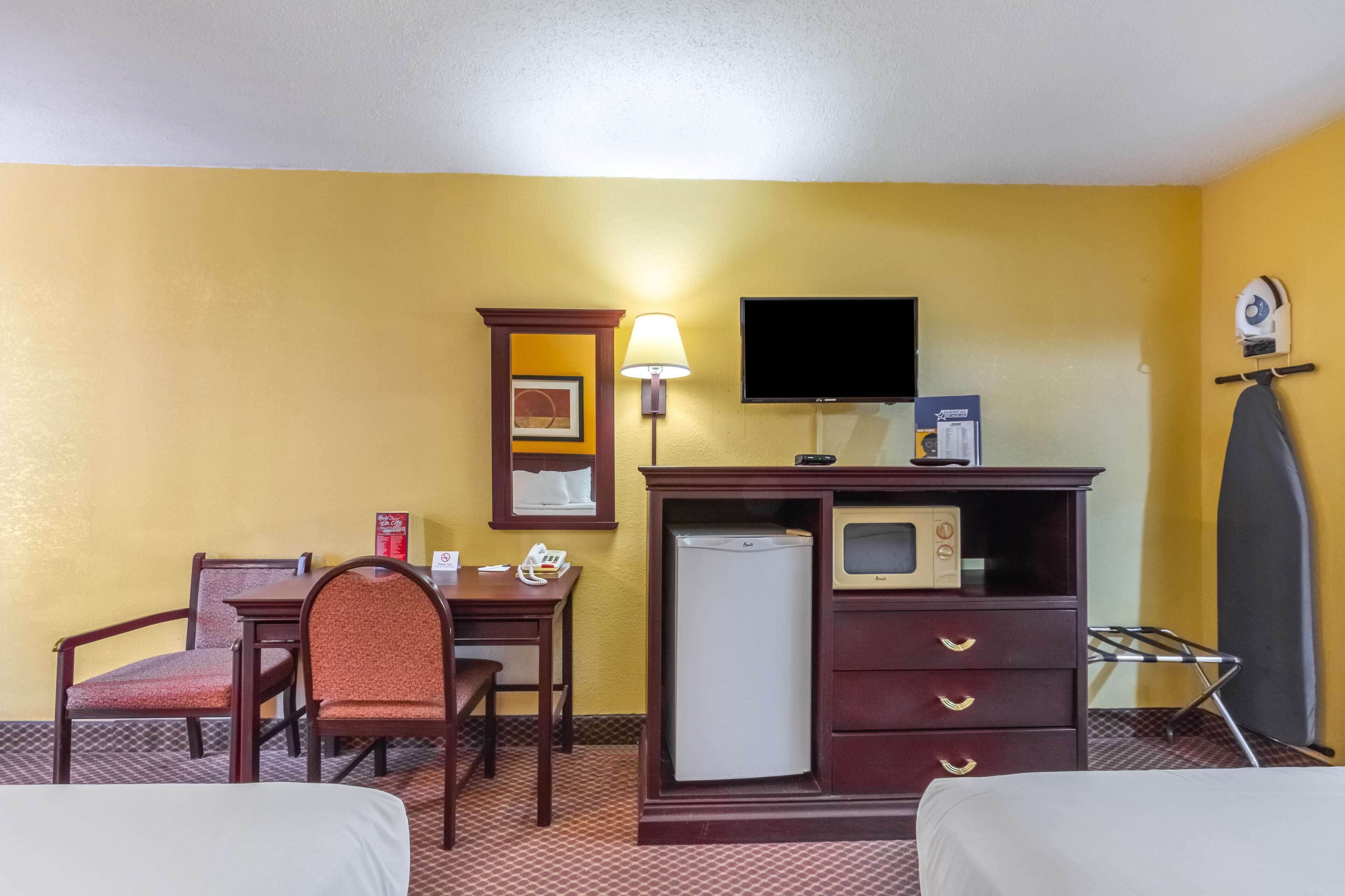A hotel room with a bed, a desk with a chair, a microwave, a refrigerator, a TV, and a lamp.