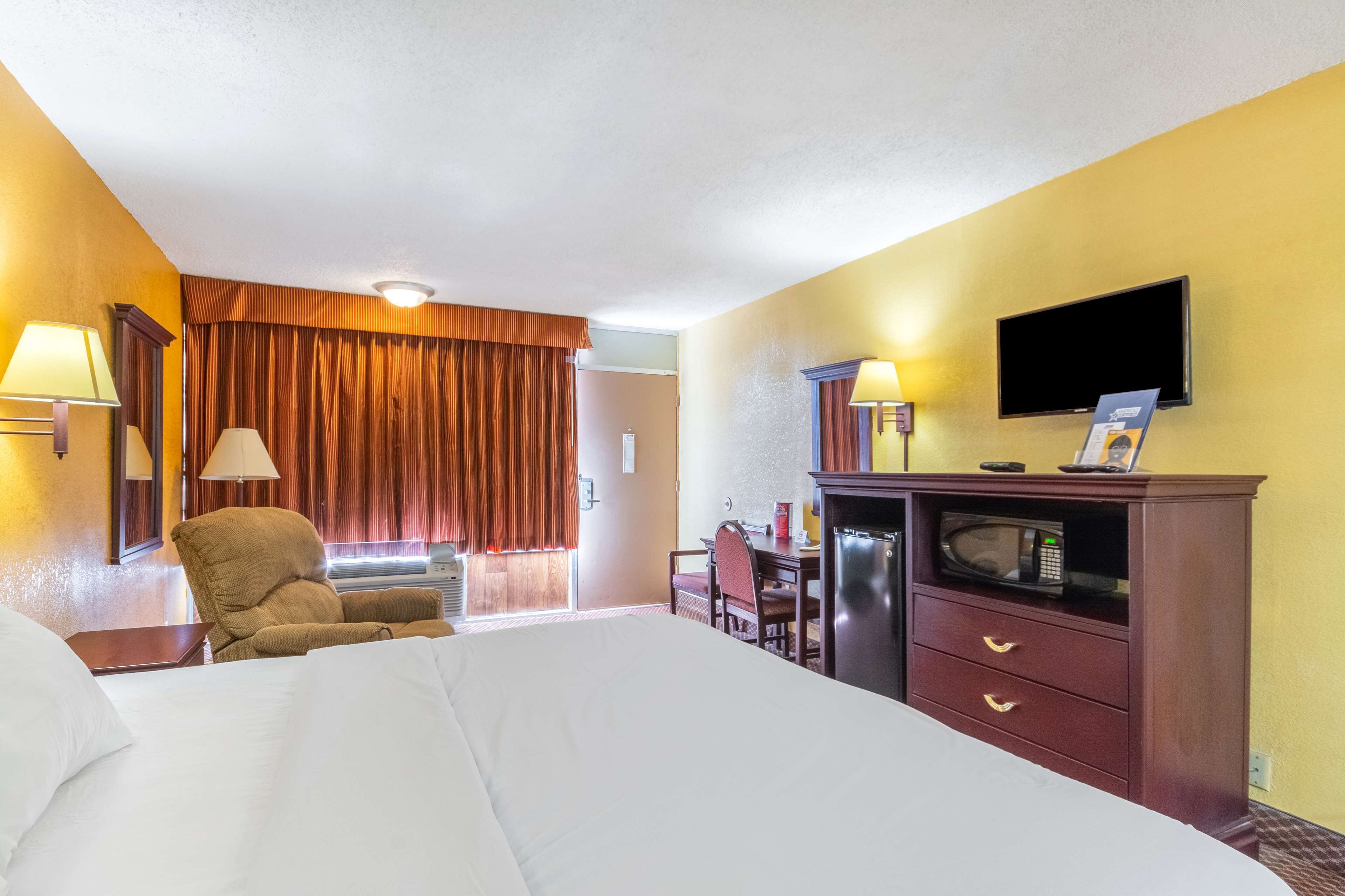 A hotel room with a large bed, a desk with a chair, a television, and a microwave.
