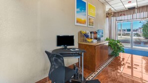 Zona de recepción con escritorio, computadora, silla y ventanal con vistas a edificios y vegetación.