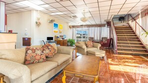 Amplia sala de estar con un conjunto de sofás, una mesa de centro, un televisor y una escalera que sube a un nivel superior.