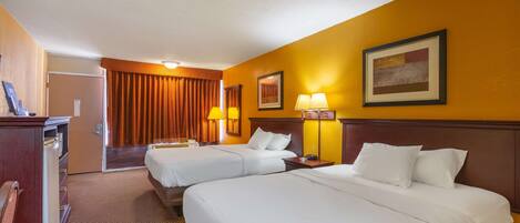A hotel room with two beds, a desk, and a chair. There are two lamps on the desk and a picture on the wall.
