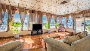 Amplia sala de estar con televisión, asientos cómodos, ventanas grandes con cortinas y vistas al exterior.