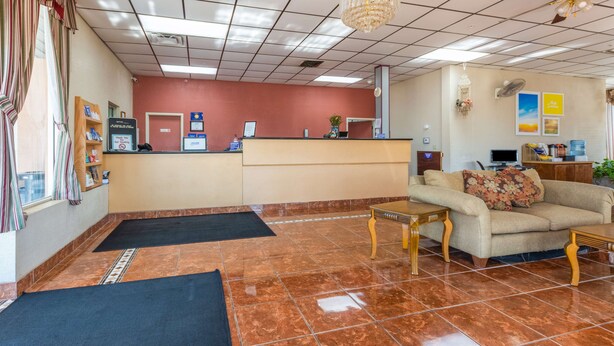 Un vestíbulo de hotel con una recepción, un sofá, una mesa de madera, una araña y un suelo de baldosas.