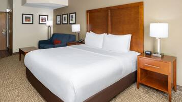 A hotel room with a large bed, a bedside table with a lamp, a chair, and a desk with a phone.