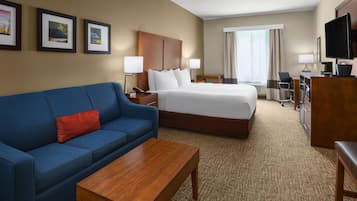 A hotel room with a bed, a blue sofa, a wooden coffee table, a desk with a chair, a television, and framed pictures on the wall.