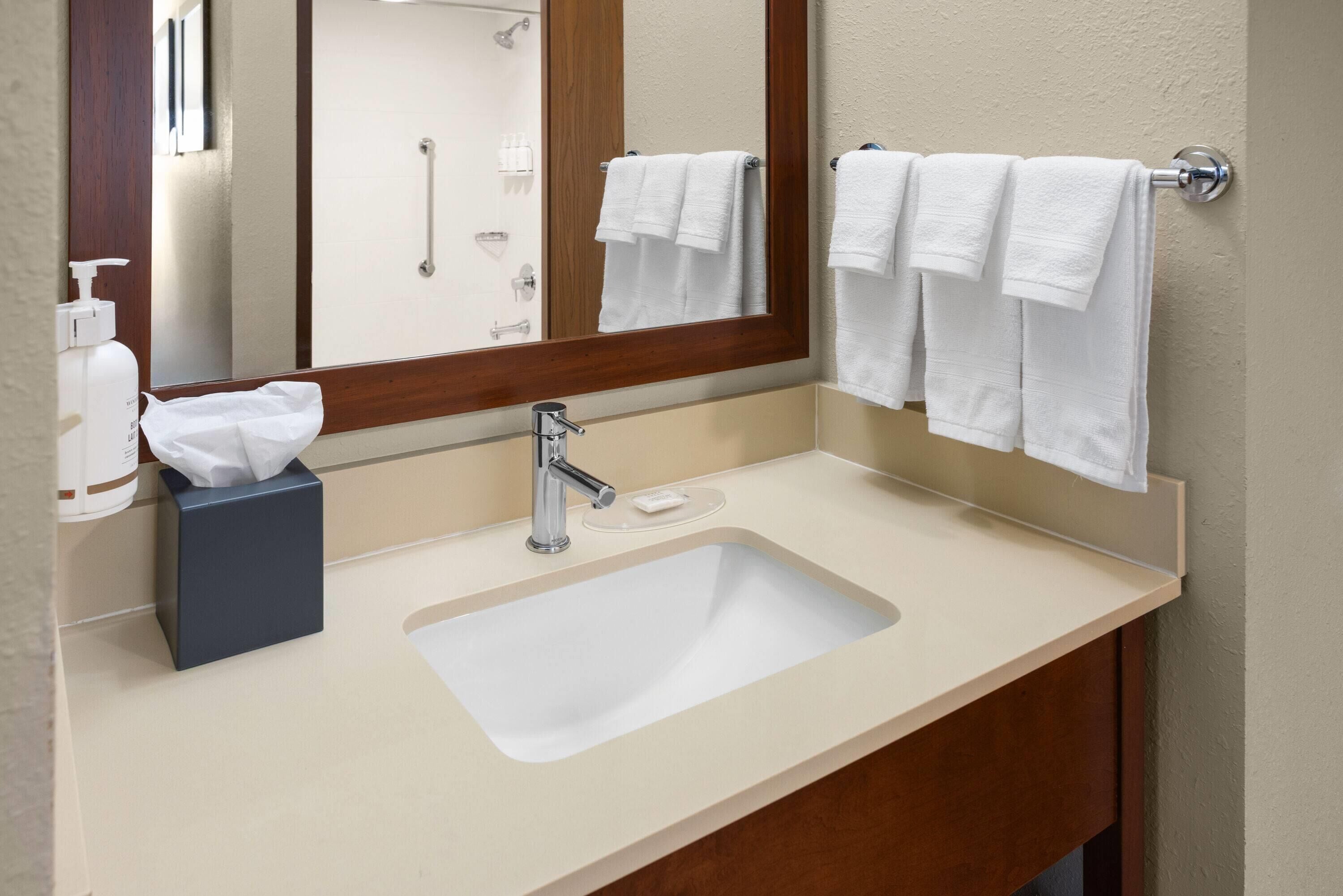 Un baño con lavamanos, espejo, toallero y artículos de aseo.