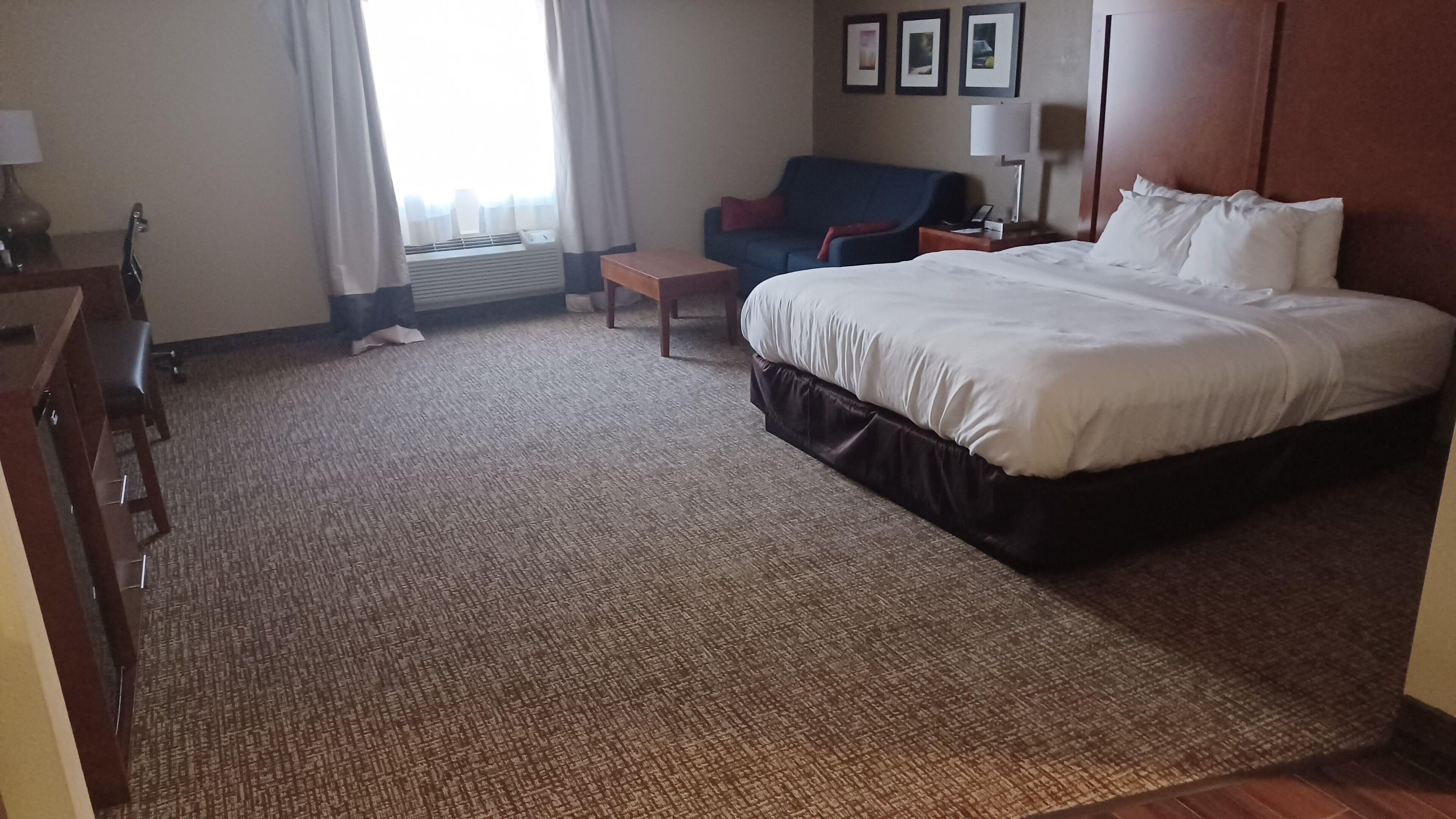 Quarto de hotel com uma cama grande, uma escrivaninha, uma cadeira, uma mesinha de centro e um sofá.