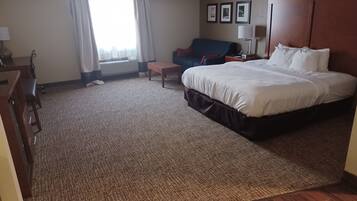 Quarto de hotel com uma cama grande, uma escrivaninha, uma cadeira, uma mesinha de centro e um sofá.