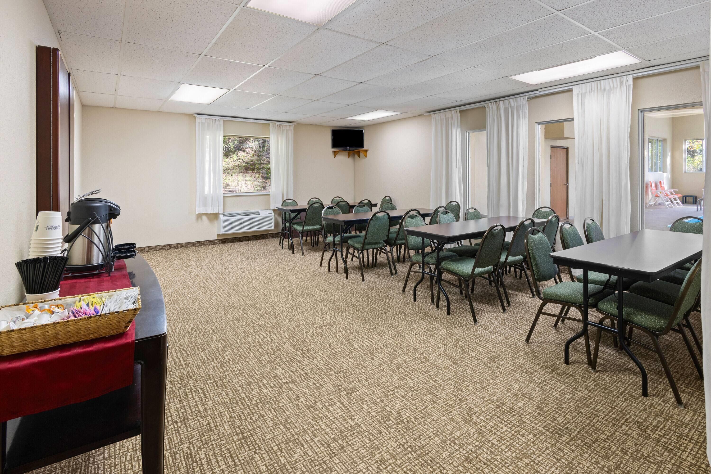 A conference room with a long table and chairs, a television on the wall, and a window with curtains.
