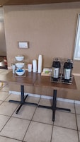A breakfast bar with coffee and water dispensers, a sign saying "less is more unless it's coffee", and a tray with bowls and cups.