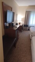 A hotel room with a bed, a desk, a television, a lamp, and a window with curtains.