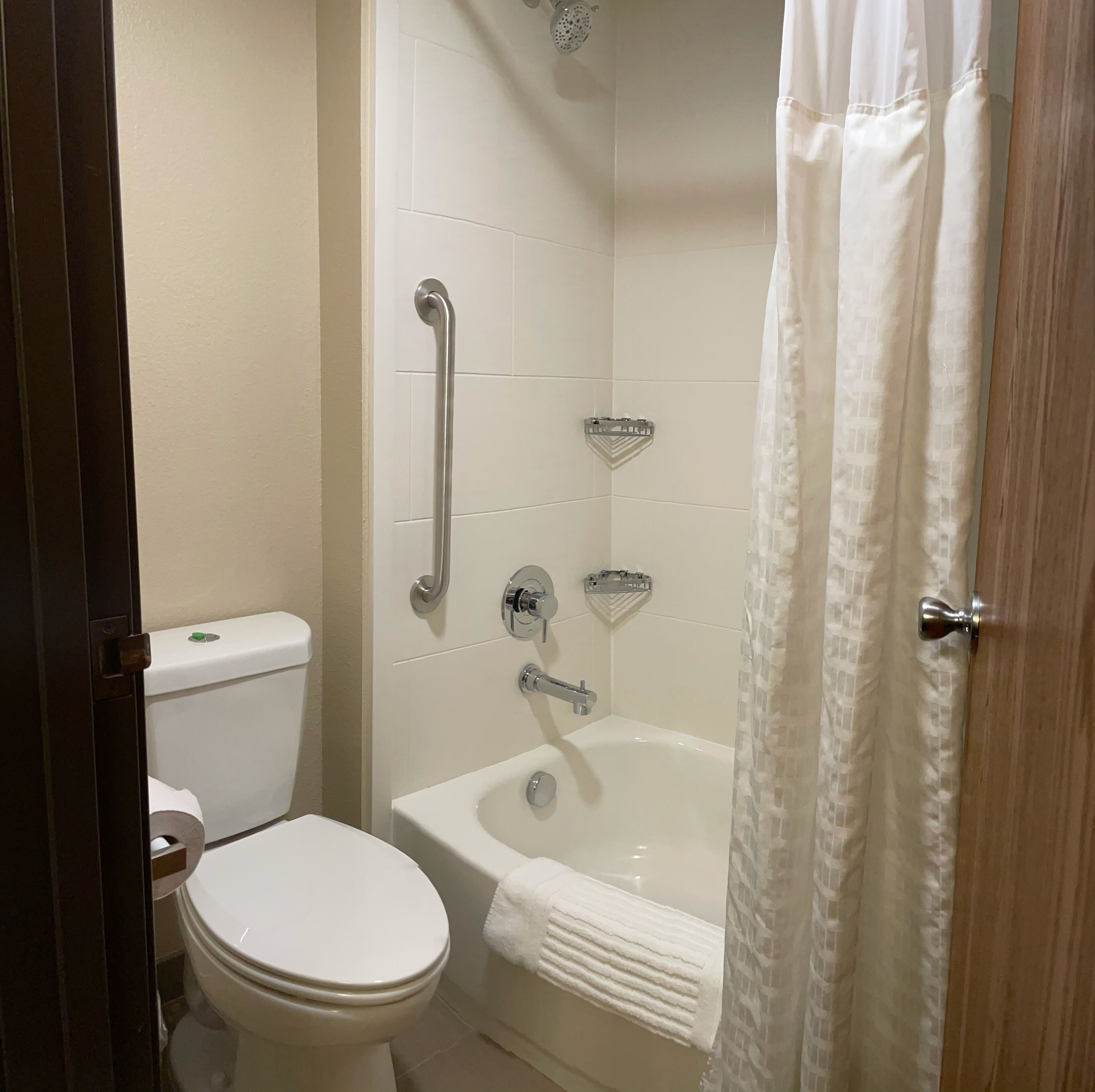 Un baño con inodoro, ducha con barra de apoyo y bañera con toalla.