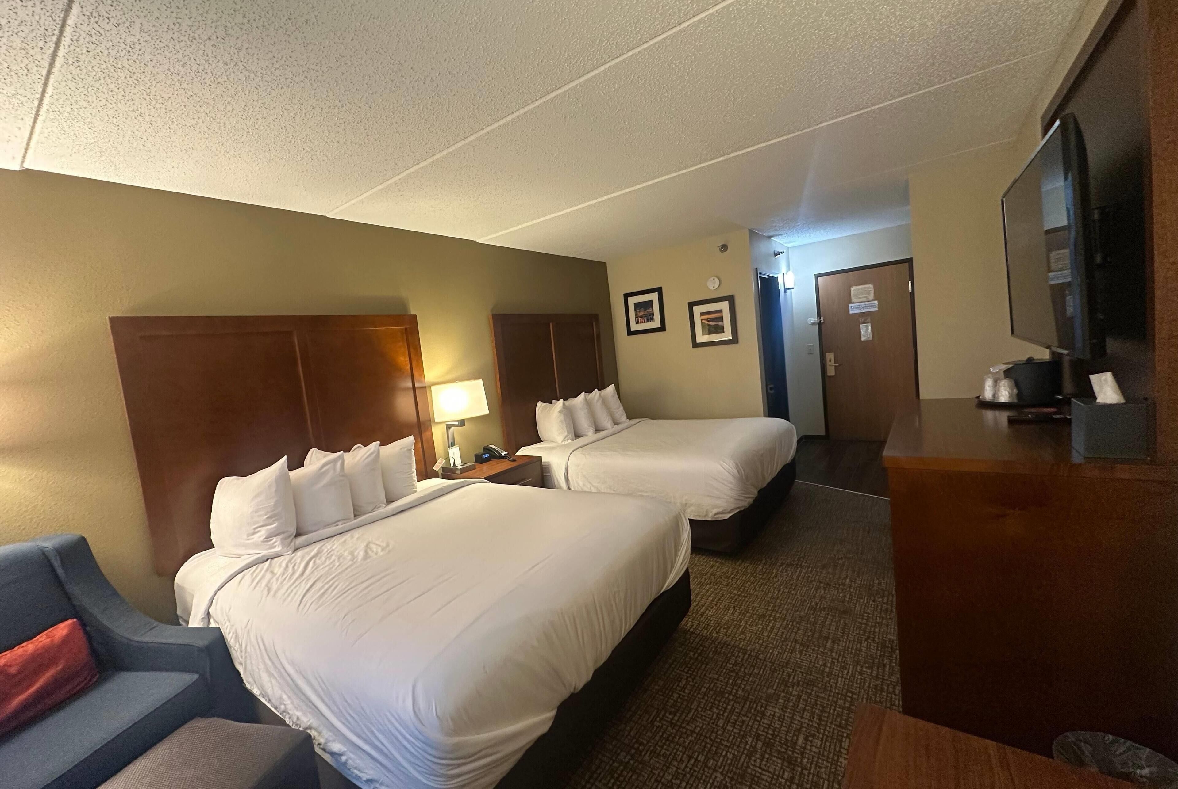 A hotel room with two beds, a desk, a TV, and a couch.