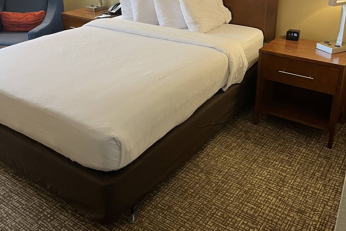 Hotellihuone, jossa on suuri sänky, kaksi yöpöytää, tuoli ja lamppu.
