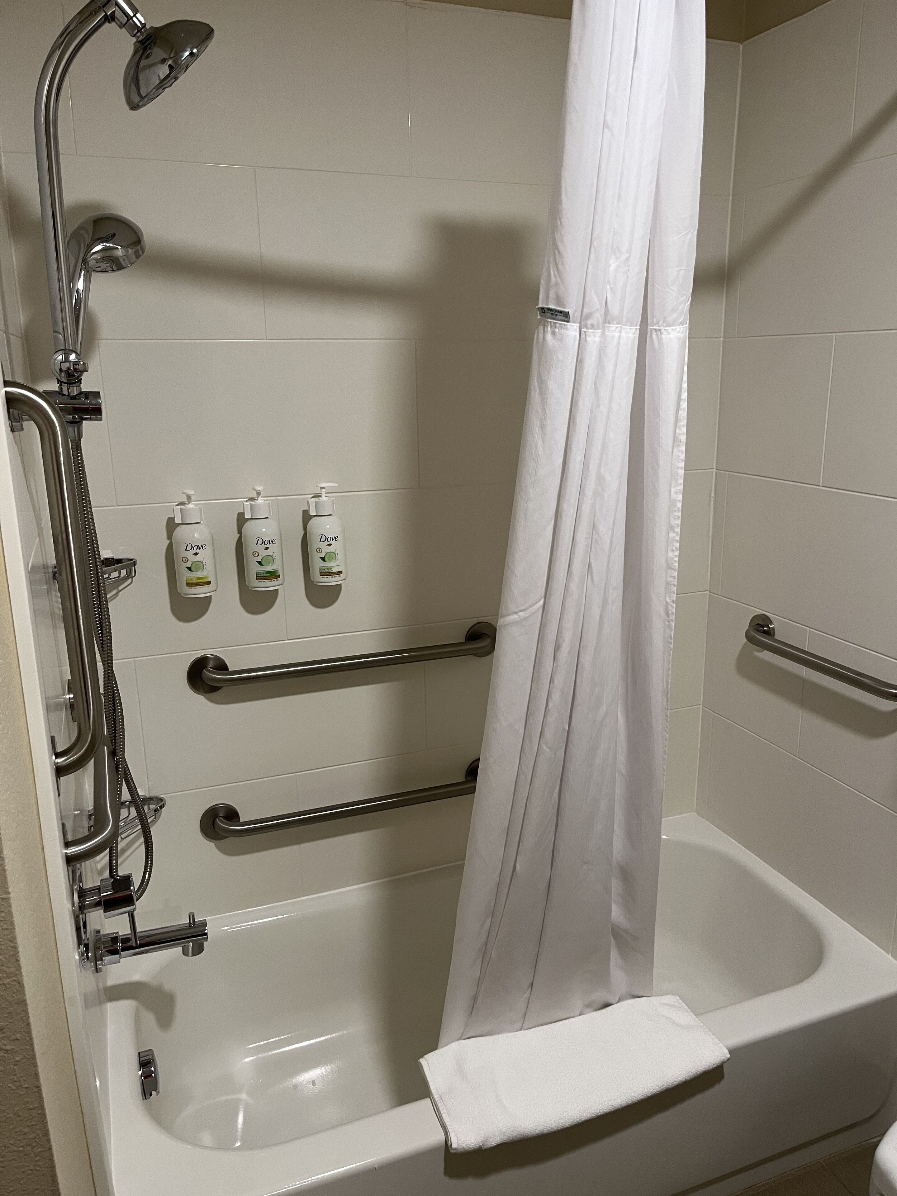A white bathtub with a shower head, grab bars, and a towel.