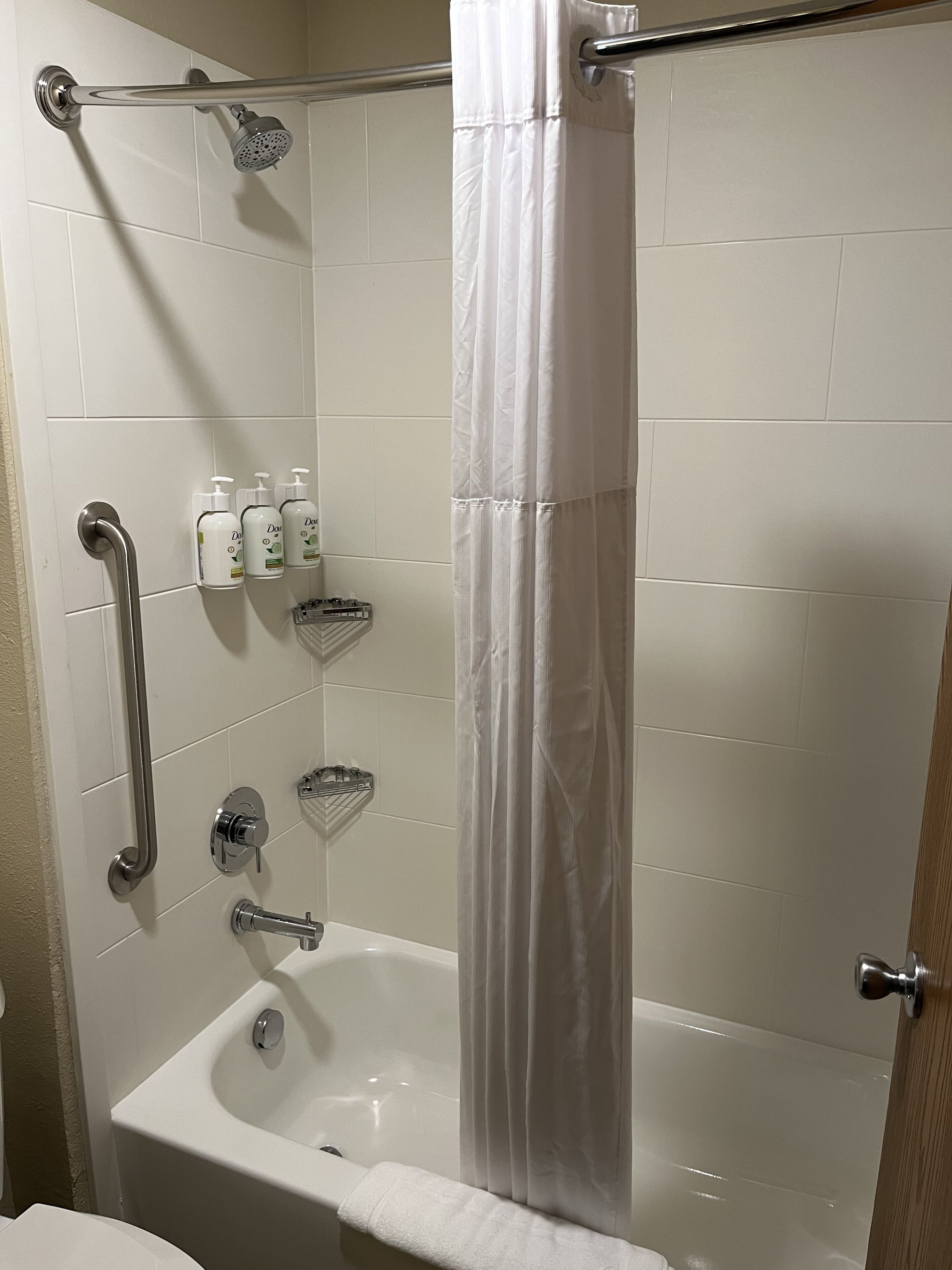 A bathroom with a bathtub, a shower with a handheld showerhead, a grab bar, a towel rack, and a shelf with toiletries.