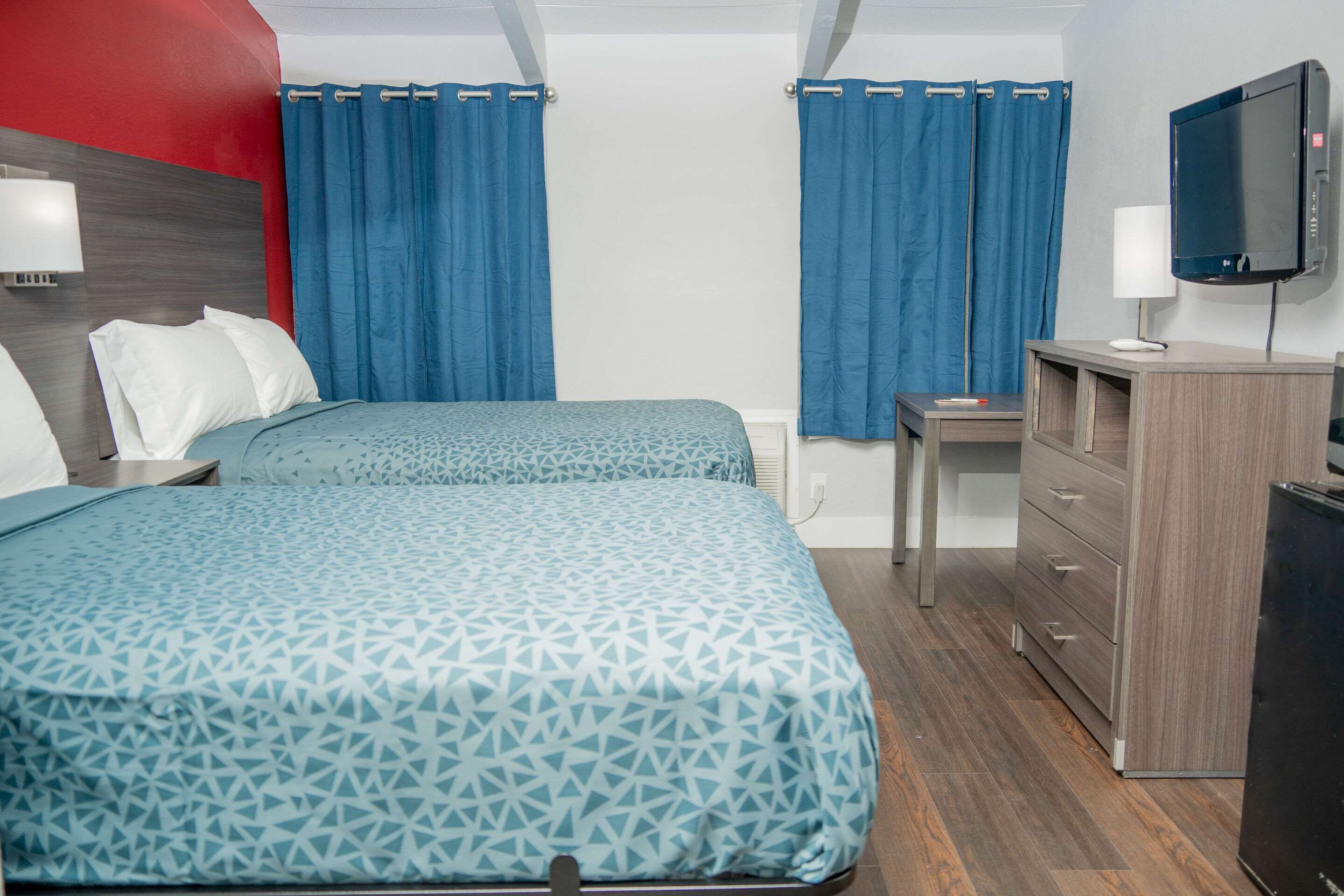 A hotel room with two beds, a desk, a TV, and a dresser.
