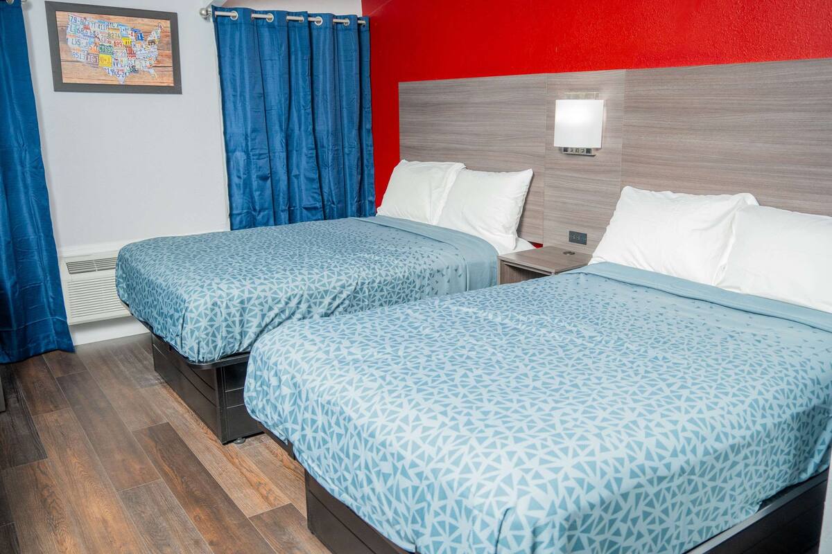 A hotel room with two beds, blue patterned bedding, a red accent wall, and a framed map on the wall.