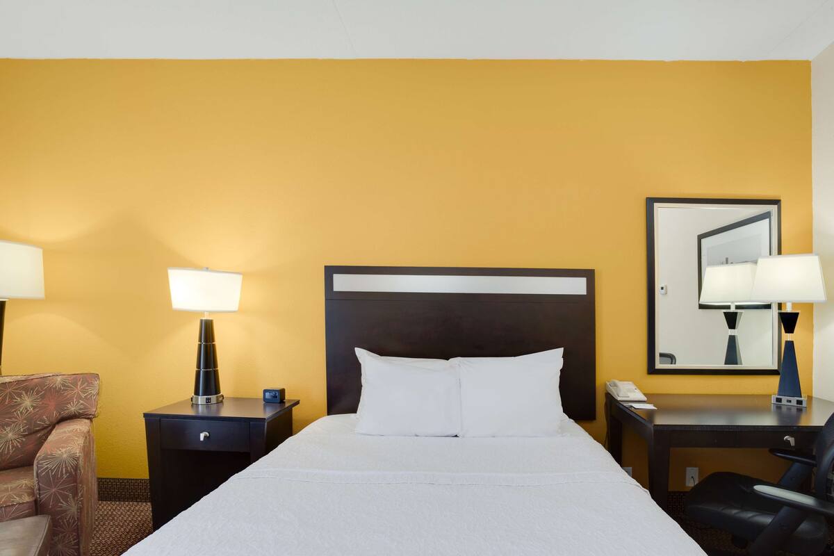 A hotel room with a bed, a nightstand, a desk, a chair, and a lamp.