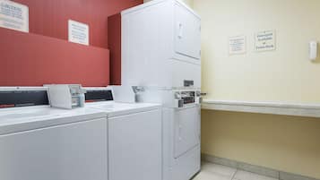 A laundry area with commercial washers and dryers, caution signs, and a detergent sign at the front desk.