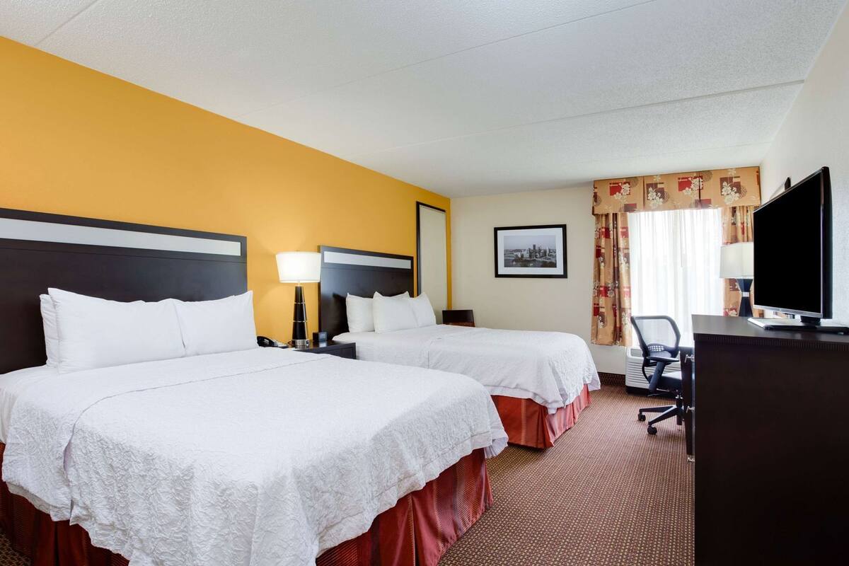 A hotel room with two beds, a desk, a television, and a framed picture on the wall.