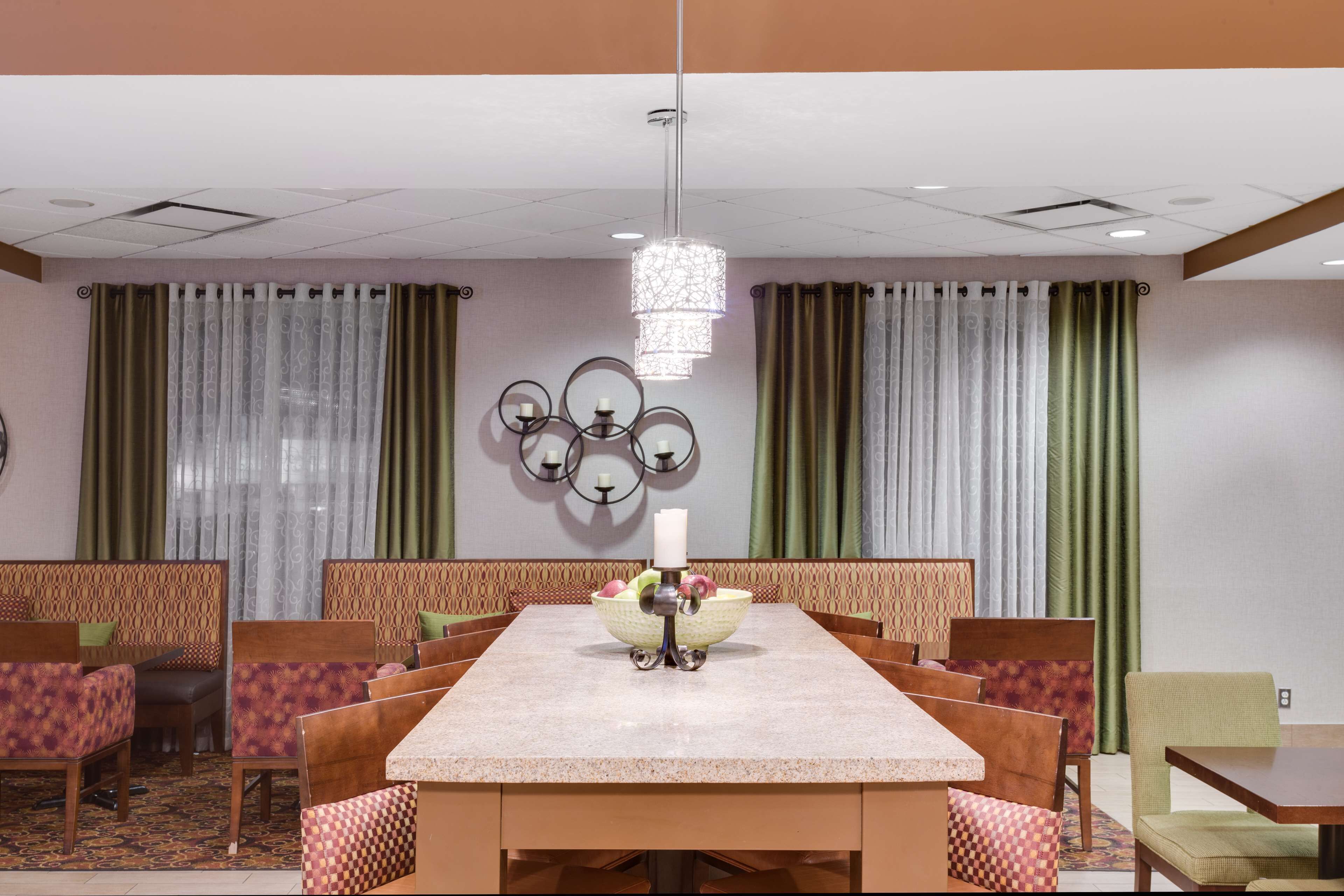 A hotel dining area with a long table, multiple chairs, a chandelier, and decorative wall sconces.