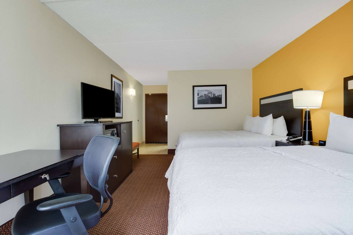 A hotel room with a bed, desk, chair, television, and a lamp.