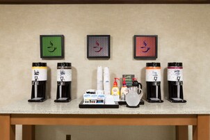 Una estación de café con varios dispensadores, una selección de cápsulas y un refrigerador pequeño.