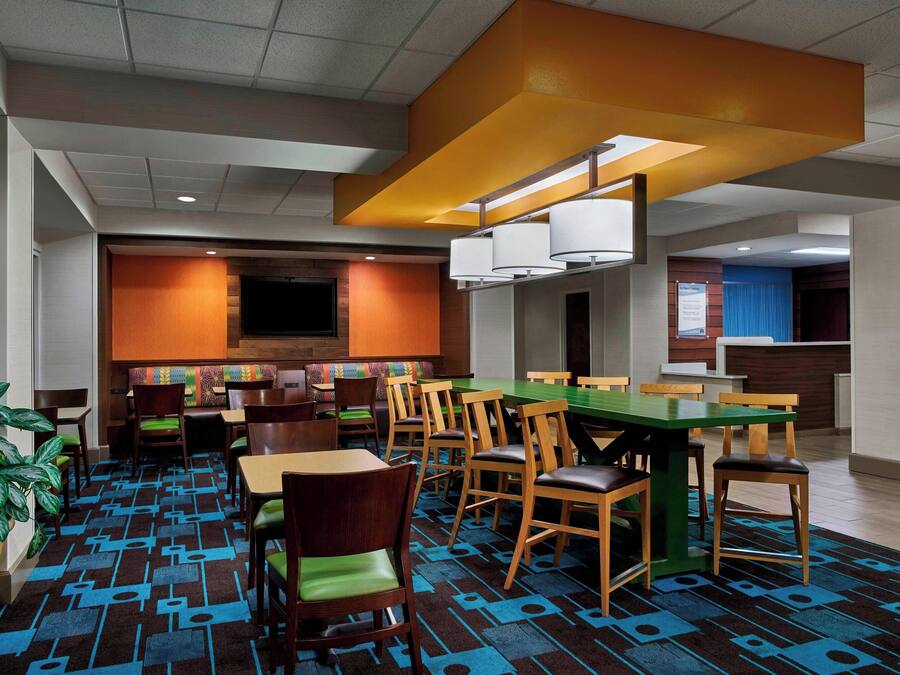 A hotel dining area with multiple tables and chairs, a large green table, and a patterned carpet.