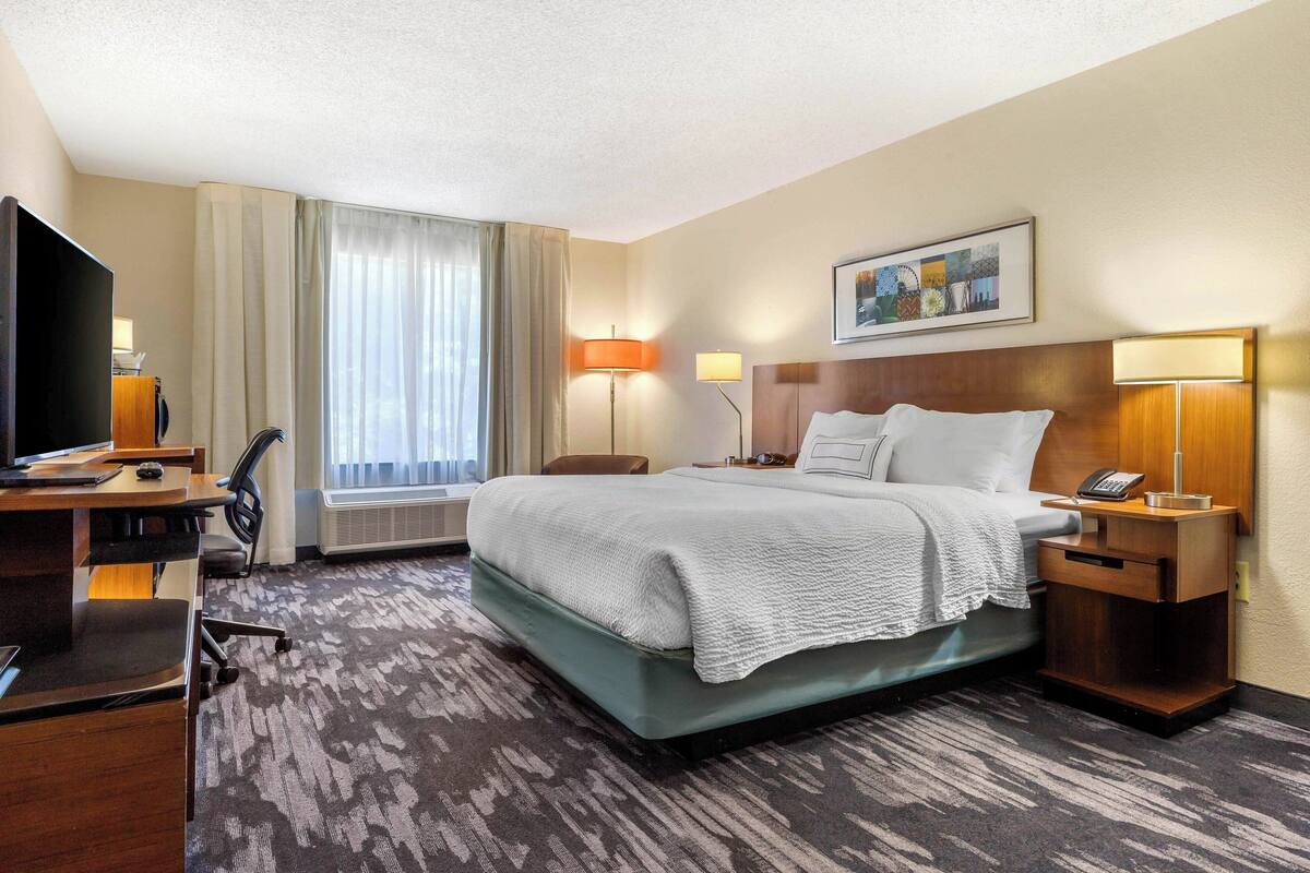 A hotel room with a bed, desk, chair, and a television.