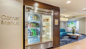 A corner market with a refrigerator stocked with beverages and snacks, a blue sofa, and a small table with a plant. - Fairfield Inn by Marriott Myrtle Beach North (Myrtle Beach)