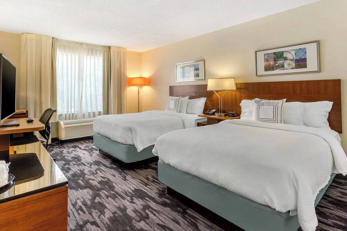 A hotel room with two beds, a desk, a TV, and a window with curtains.