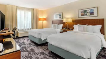 A hotel room with two beds, a desk, a TV, and a window with curtains.