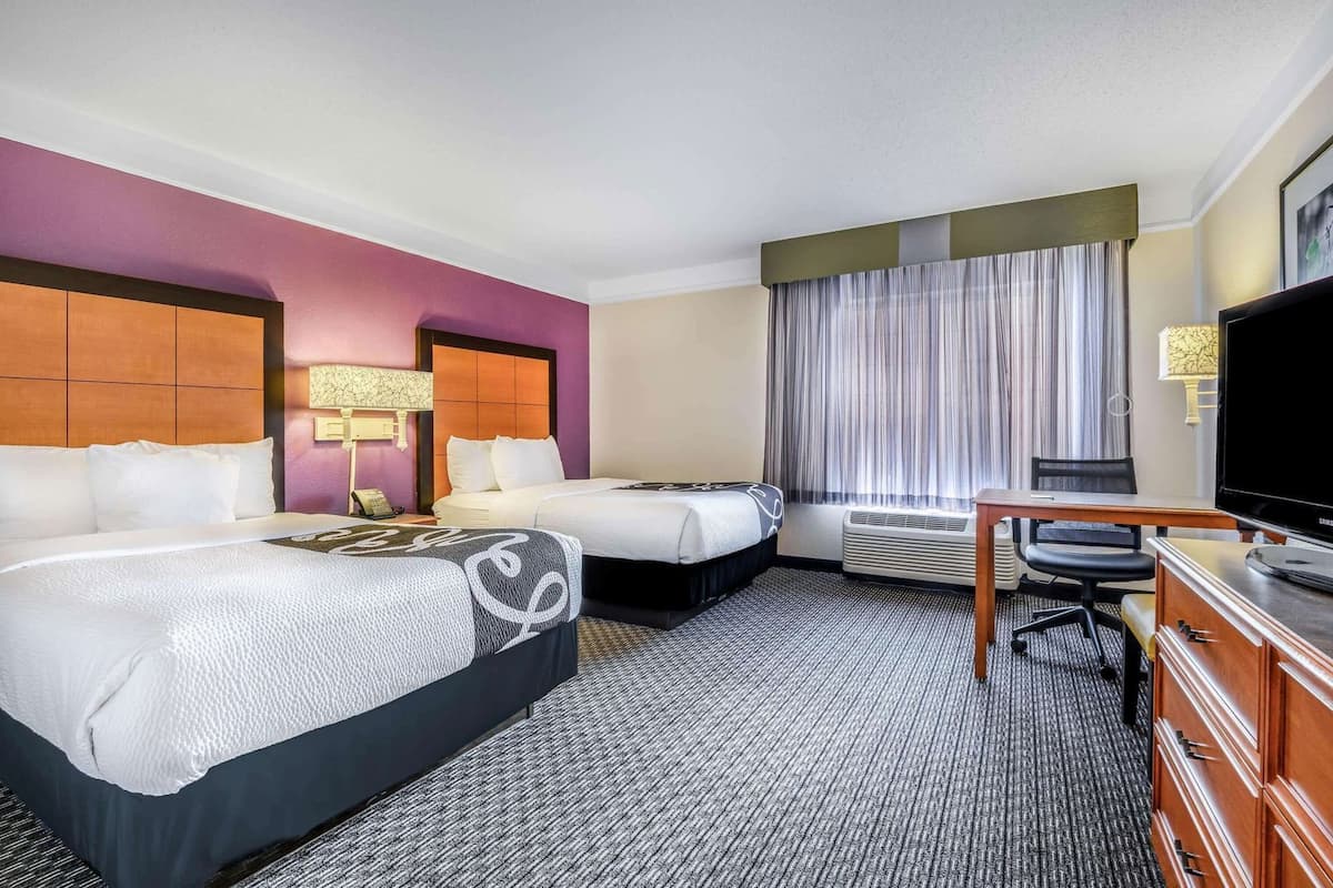 A hotel room with two beds, a desk, a television, and a window with curtains.