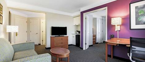 A hotel room with a sofa, a TV, a desk, and a chair.