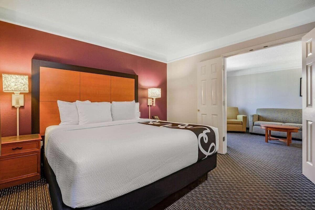 A hotel room with a large bed, two bedside lamps, a wooden nightstand, a sofa, and a small table.