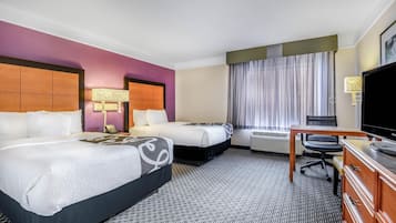 Habitación de hotel con dos camas, un escritorio, un televisor y una ventana con cortinas.
