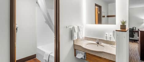 A modern bathroom with a wooden floor, a bathtub, a shower with a curtain, a sink with a mirror, and a small potted plant.