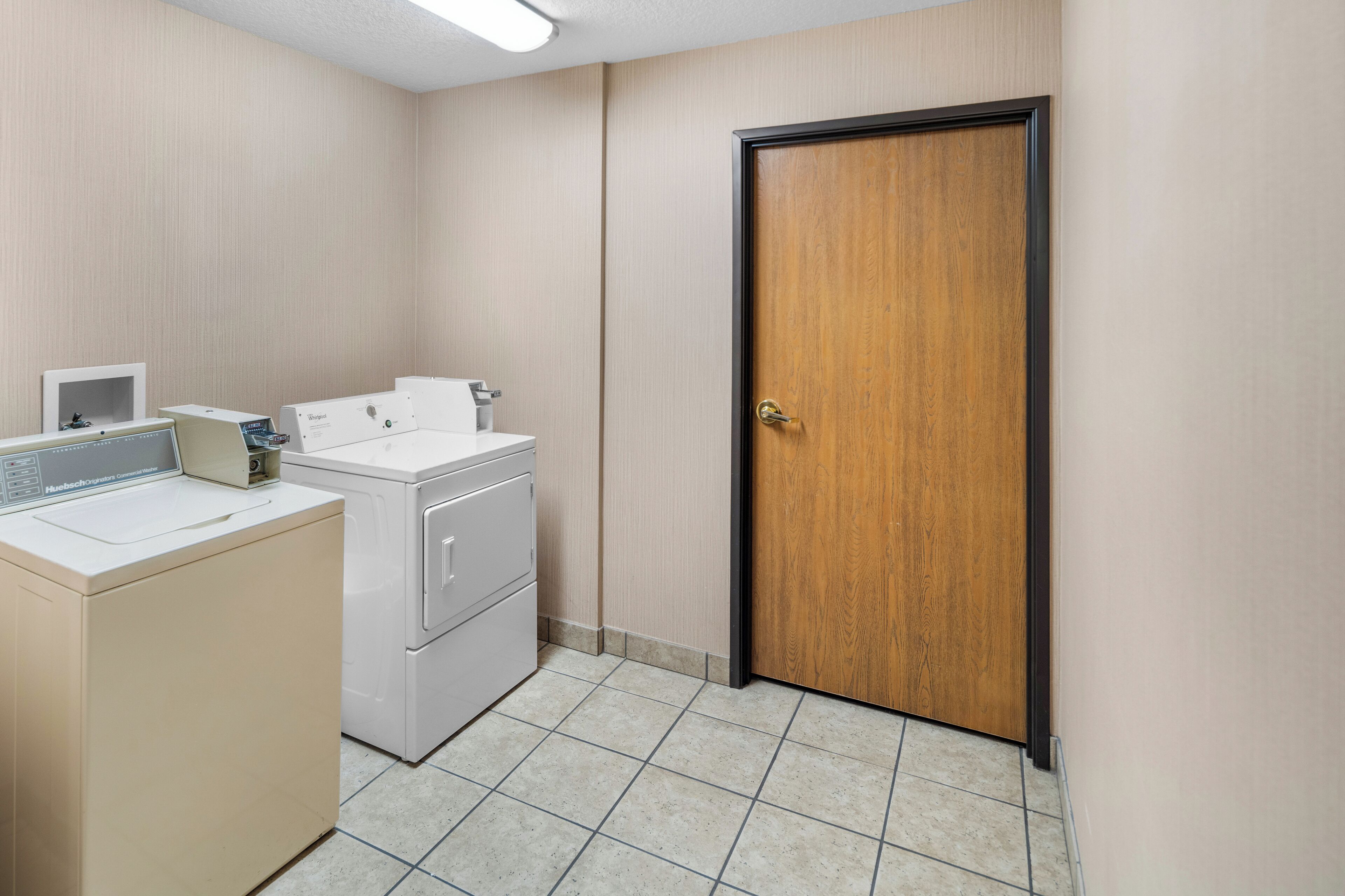 A laundry room with a washing machine, dryer, and a wooden door.