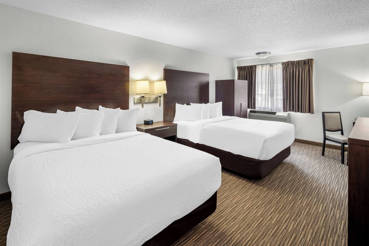 A hotel room with two beds, a desk, a chair, and a large window with curtains.