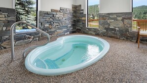 An indoor swimming pool with stone walls and a view of a forested area. - EverSpring Inn & Suites (Hill City)