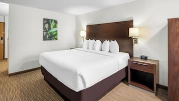 A hotel room with a large bed, two bedside tables, a wooden headboard, a wall-mounted lamp, and a clock.