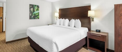 A hotel room with a large bed, two bedside tables, a wooden headboard, a wall-mounted lamp, and a clock.