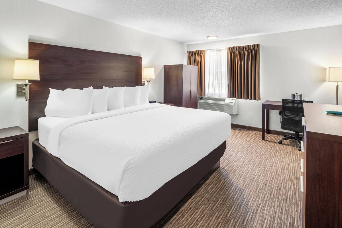 A hotel room with a large bed, a desk, a wardrobe, and a window with curtains.