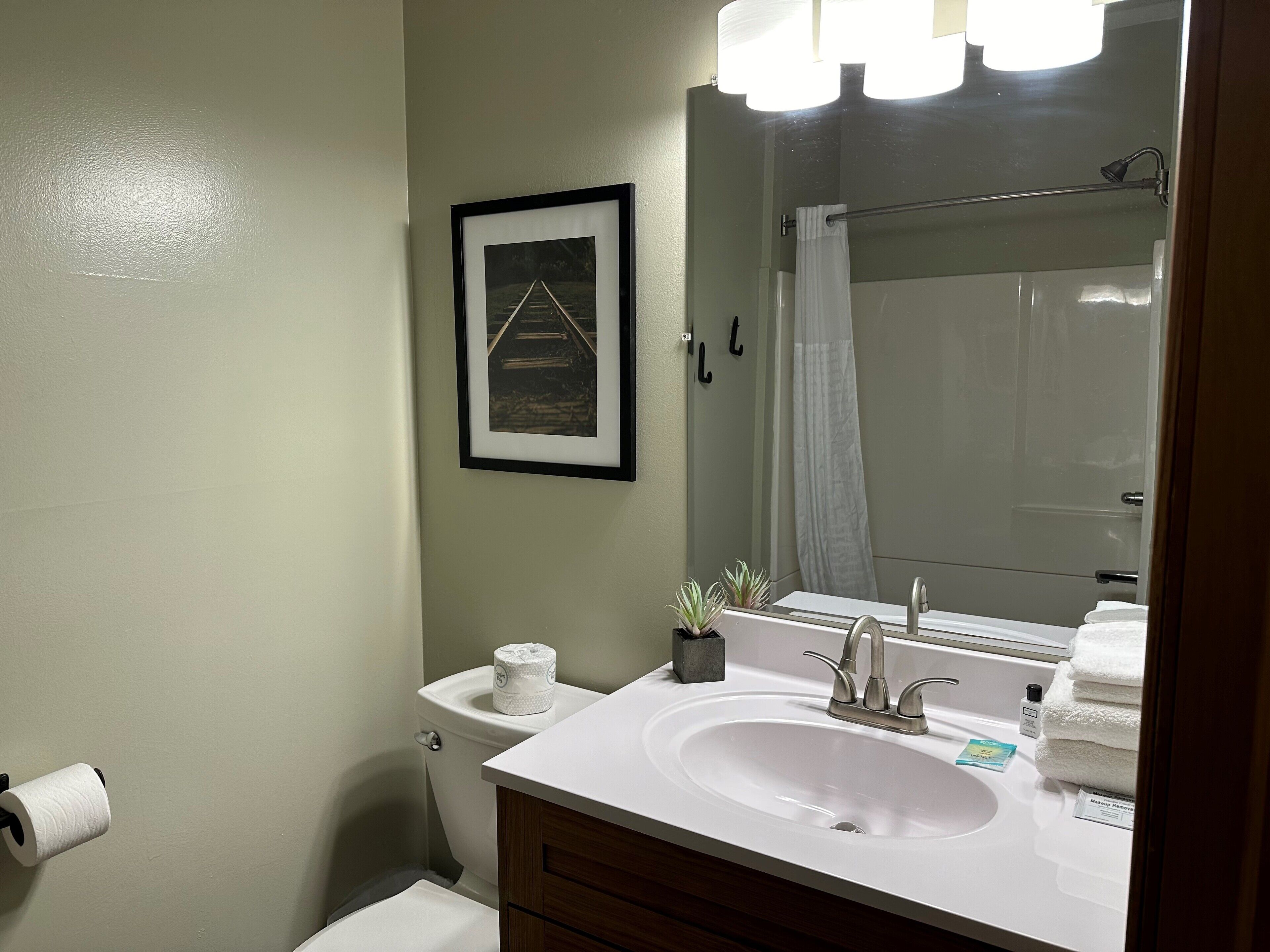 A bathroom with a white sink, a framed picture on the wall, a toilet, and a shower area.