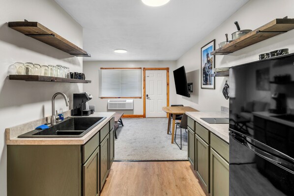 A compact kitchen with a sink, countertop, wooden cabinets, a dining table, and a TV mounted on the wall.