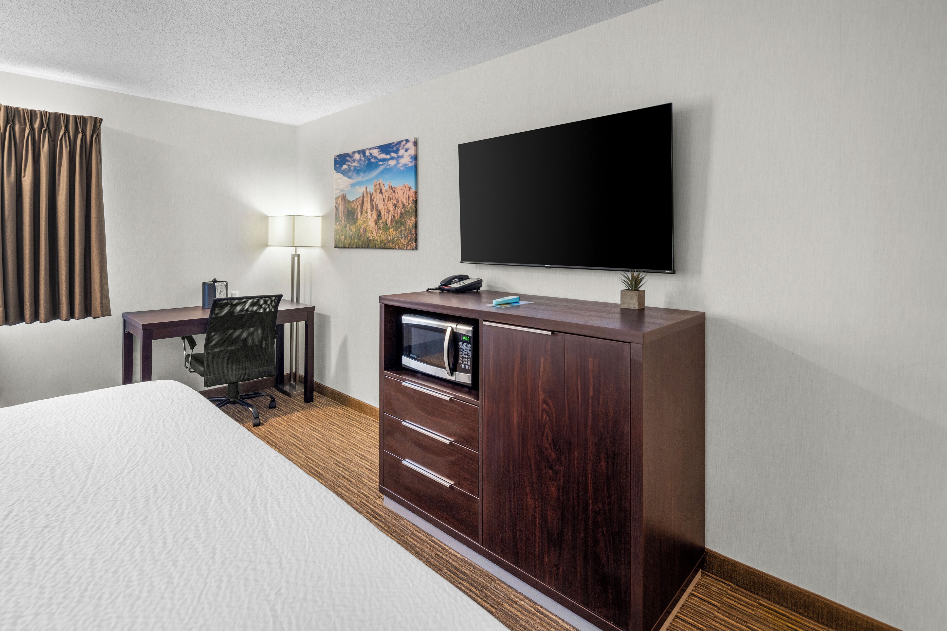 A hotel room with a bed, a desk with a computer, a flat-screen TV, a lamp, and a painting on the wall.
