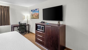 Habitación de hotel con una cama, un escritorio con computadora, un televisor de pantalla plana, una lámpara y un cuadro en la pared.